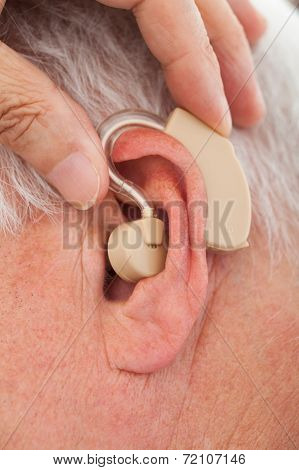 Doctor Inserting Hearing Aid In Senior Man's Ear