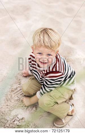 Beautiful blonde boy playing with sand on the beach