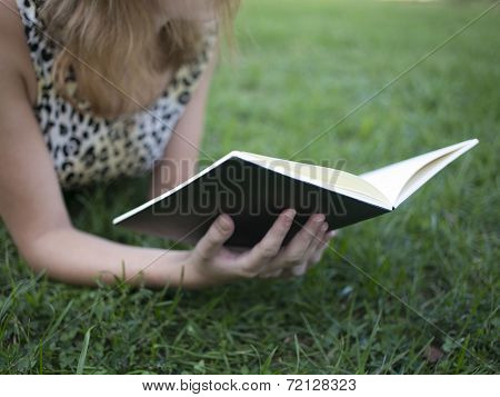 Girl reading book and lying on grass in the summer park