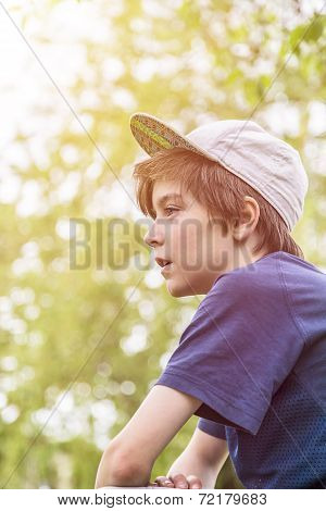 Profile Of A Young Boy With Base Cap And Blurred Green Leafs In Background