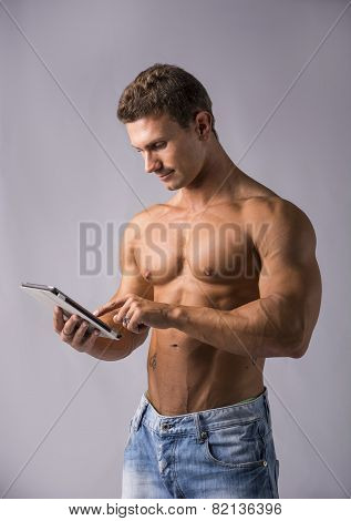 Shirtless young male bodybuiler holding ebook reader or tablet PC