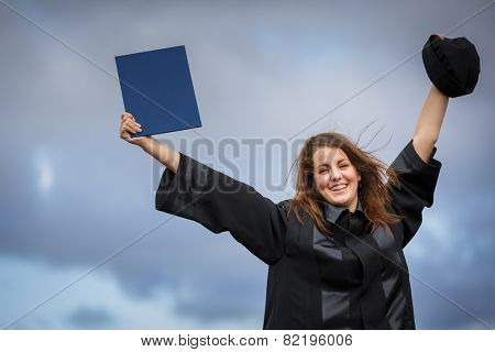 Pretty, young woman celebrating joyfully her graduation - spreading wide her arms, holding her diploma, savouring her success (color toned image; shallow DOF)