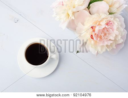 Still life with cup of coffee and flowers (peonies) on light blue wooden table.