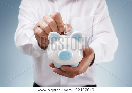 Businessman inserting a coin into a piggy bank concept for business savings, investment or banking