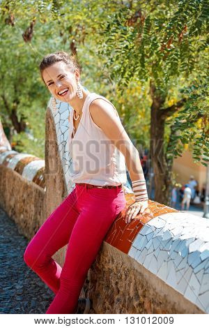 Smiling Woman Sitting On Trencadis Style Fence In Park Guell