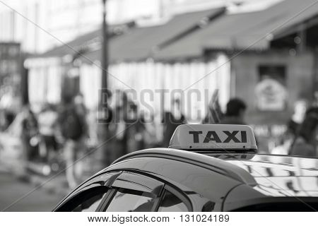 symbol or sign with an inscription of a taxi is located on a car roof on an indistinct background street of monochrome color