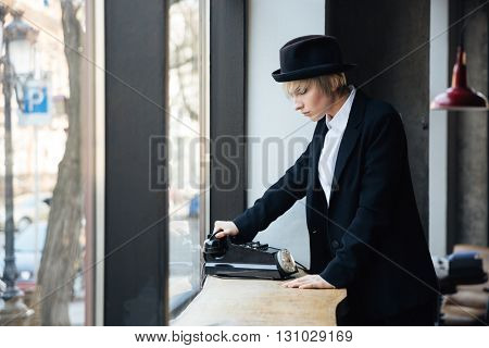Beautiful young woman in hat dusing old telephone in cafe