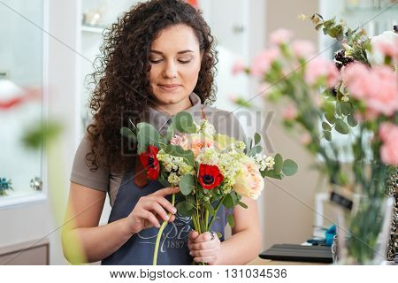 Thoughtful cute young woman florist holding flowers and making bouquet in shop