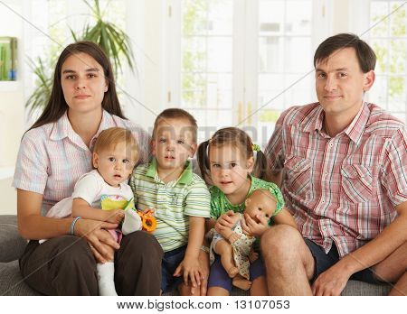 3 Çocuklu evde koltukta oturan kameraya, seyir mutlu çekirdek aile portresi gülümseyen