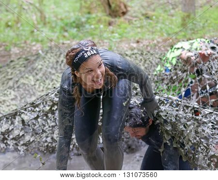 STOCKHOLM SWEDEN - MAY 14 2016: Smiling beautiful woman with braids covered with mudfighting to get out of a camouflage net in the obstacle race Tough Viking Event in Sweden April 14 2016