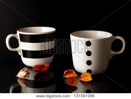 Two tea cups on a black background with dried flowers