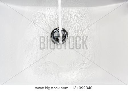 Fresh water running down the drain of a ceramic washbasin