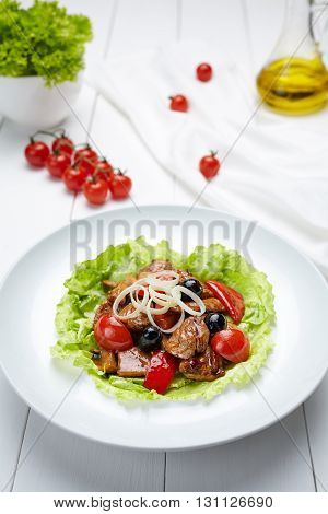 Grilled pork warm salad with sauce, tomatoes, champignon mushrooms, pepper and leek onion. Restaraunt menu meal in white dish on table background