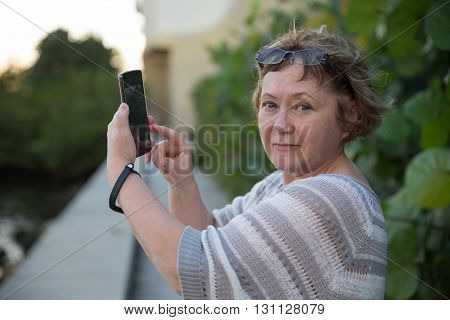 Pretty adult woman photographing by telephone looking at camera