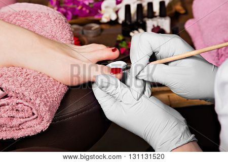 Closeup finger nail care by pedicure specialist in beauty salon. Pedicurist clear cuticle professional scissors for manicure and pedicure.