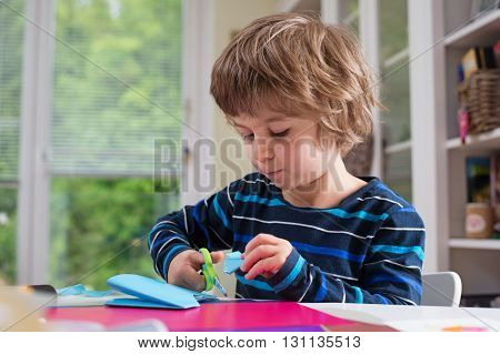 Cute litle boy cutting shapes out of colored paper. Being creative developing imagination creativity do it yourself concept