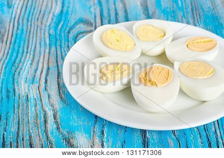 Boiled hen eggs in a white plate on a blue wooden background