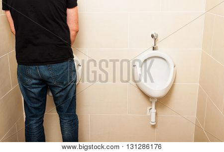 Man standing in front of a white pissoir in a public modern bathroom