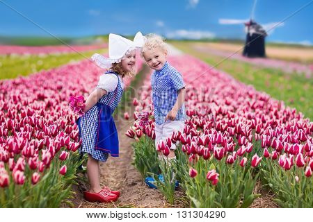 Happy Dutch children playing in blooming tulip flowers field. Boy and girl wearing traditional national costume wooden clogs and hat play with tulips next to a windmill in Holland Netherlands