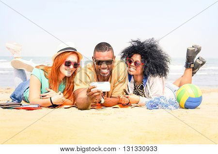 Multiracial friends having fun taking selfie lying on the beach - Happy multiethnic students watching video on line - Concept of youth friendship and addiction to new mobile phone technologies