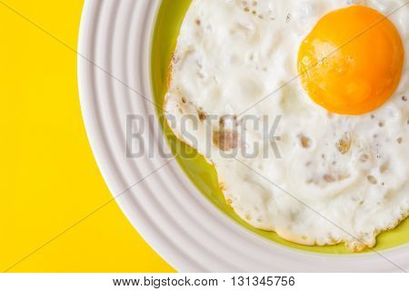 Fried egg on white-green plate on yellow background. Top view.