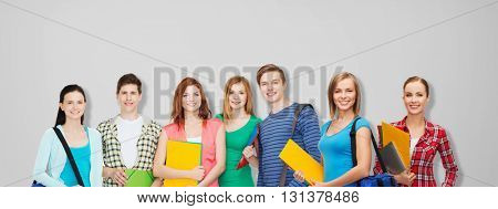 education, school and people concept - group of smiling teenage students with folders and school bags over gray background