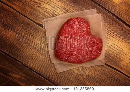 Raw heart shaped burger cutlet over grunge wooden background. Toned image. Top view