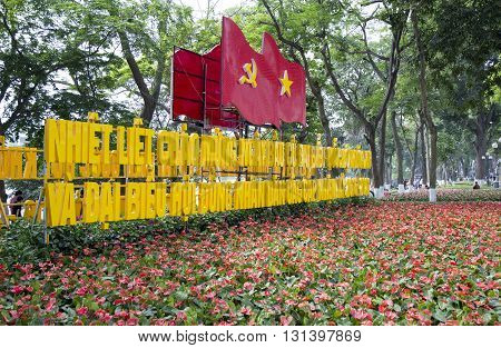 Hanoi, Vietnam - May 21, 2016: Vietnamese flag along with communist flag and a communicational message from the party and government in a floral garden at the bank of Hoan Kiem (Sword) lake.