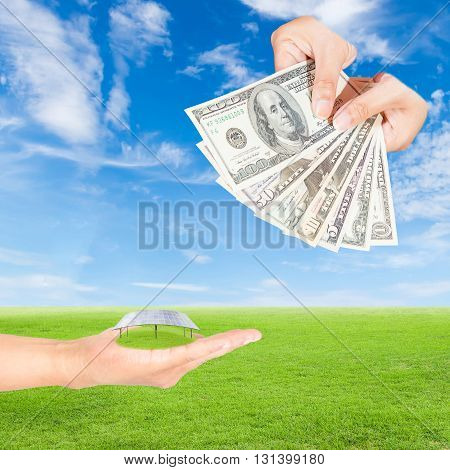 Carbon credits concepthand holding solar panels and US Dollars banknote against green field and blue sky background