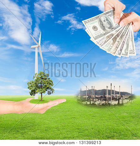 Carbon credits concepthand holding tree and wind turbine and US Dollars banknote with oil refinery plant against green field and blue sky background