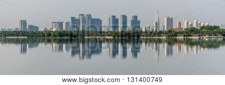 Panorama of the city and trees reflected in calm water. Wide panorama of skyscrapers on a background of clear sky. Panorama of a modern city