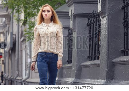 Girl walking down the street with her phone. A woman is walking alone in City. Blurred on background there are typical english houses and shops.