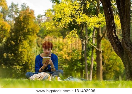 Girl reading a book. / Red-haired girl reading a book on a glade in the park.