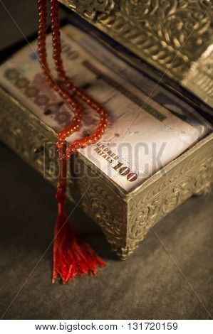 Muslim prayer beads and Saudi currency notes in vintage chest.
