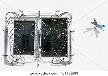 The barred window in the wall with artificial dragonfly