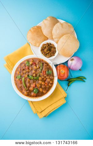 spicy chick peas also known as Chola Masala or Chana Masala or Chole served with fried puri, pickle and green salad