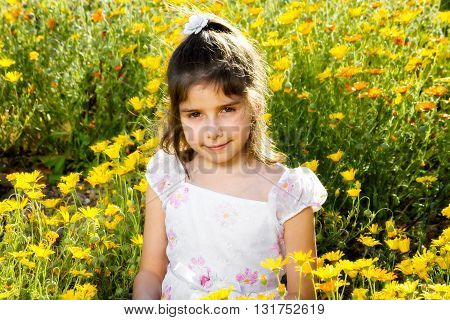 Sweet little girl with a confident closed mouth smile sitting in a bed of wild African Daisies. Her eyes are a bit red from allergies. She is backlit.