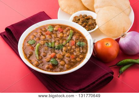 spicy chick peas also known as Chola Masala or Chana Masala or Chole served with fried puri, pickle and green salad