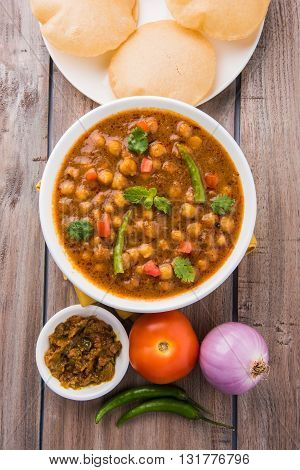 spicy chick peas also known as Chola Masala or Chana Masala or Chole served with fried puri, pickle and green salad