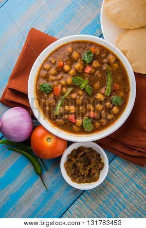 spicy chick peas also known as Chola Masala or Chana Masala or Chole served with fried puri, pickle and green salad