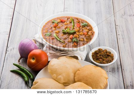 spicy chick peas also known as Chola Masala or Chana Masala or Chole served with fried puri, pickle and green salad