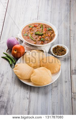 spicy chick peas also known as Chola Masala or Chana Masala or Chole served with fried puri, pickle and green salad