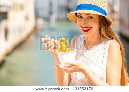 Young female traveler eating traditional italian bolognese pasta to go on the bridge in Venice. Image with small depth of field