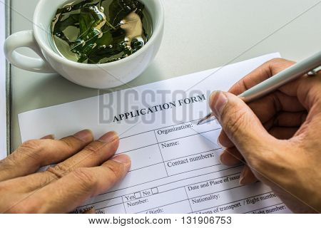 application form with tea cup.hand man Filling in the application form in black ink