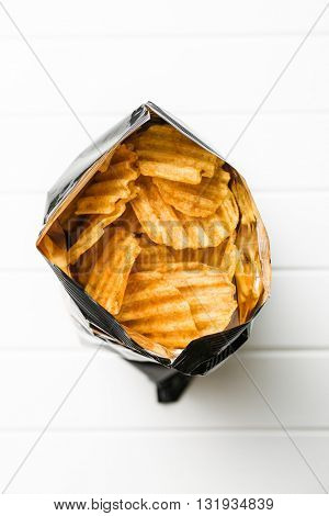 Crinkle cut potato chips on white table. Tasty spicy potato chips in bag. Top view.