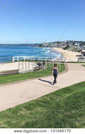 A woman walks along newly constructed coastal walkway at Bar Beach - Newcastle Australia and a beuatiful sunny Autumn day.
