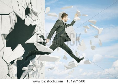 Business breakthrough success concept with businessman jumping through wall on sky background