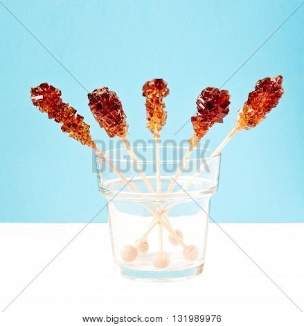 Five brown sugar stirrers in a glass on a white table with light blue background.