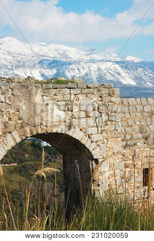 Mogren Fortress On A Seaside Hill In Budva City, Montenegro. Winter Sunny Day. Snow In Mountains