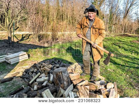 Senior Man Splitting Wood With Ax In The Garden.